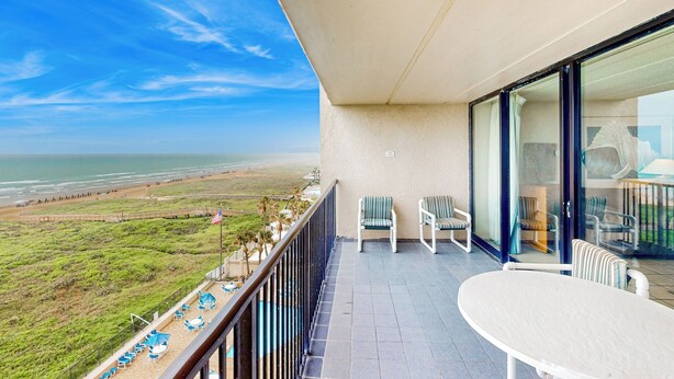 Un balcon avec vue sur la plage, deux chaises, une table et un drapeau.