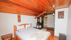 Een slaapkamer met een houten plafond, een bed met witte lakens, een nachtkastje en een spiegel.
