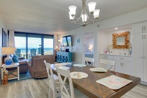 Een moderne woonkamer met een groot raam, een eethoek met een houten tafel en een keuken met witte kastjes.
