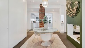 Un comedor moderno con una mesa de vidrio, sillas blancas, una pared de ladrillo y una lámpara colgante.