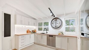 Una cocina moderna con armarios blancos, una isla central, un fregadero y un reloj en la pared.