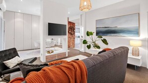 Una sala de estar moderna con un sofá gris, un televisor y un cuadro grande de un paisaje marino.