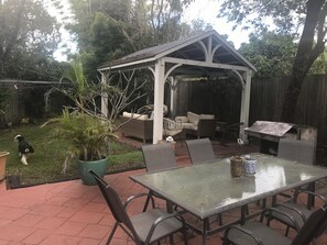 Un patio couvert comprenant une table en verre, des chaises et un espace aménagé pour s’asseoir.