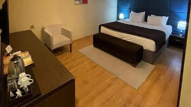 A hotel room with a bed, a desk, a chair, a chandelier, and a painting on the wall. - Tabriz iki (Baku)