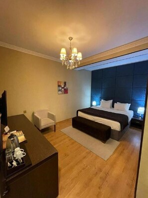A hotel room with a bed, a desk, a chair, a chandelier, and a painting on the wall. - Tabriz iki (Baku)
