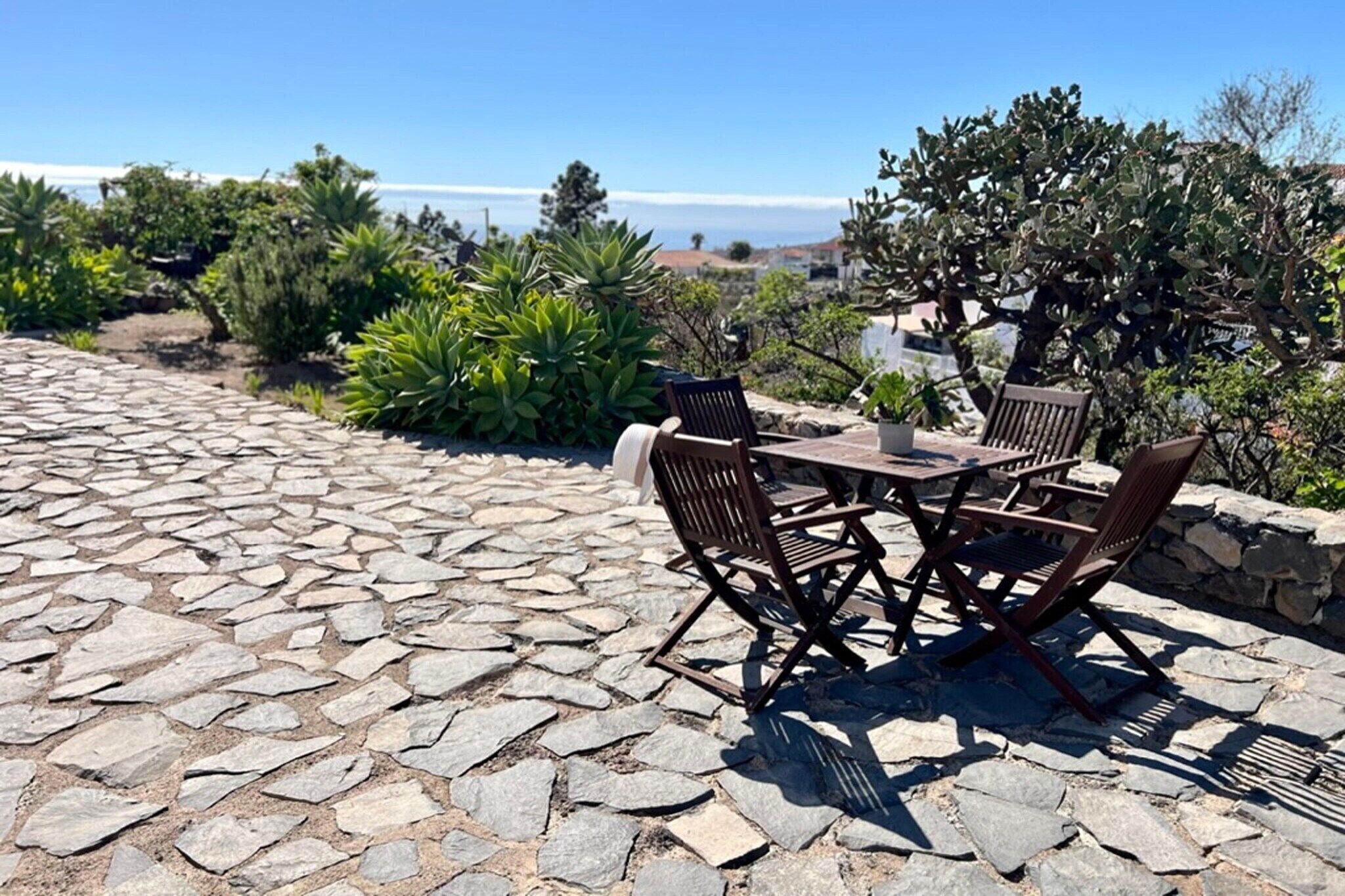 Um pátio de pedra com mesa e cadeiras, rodeado por vegetação e vista para o oceano.