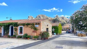 Una strada fiancheggiata da edifici, alcuni con piante e insegne, sotto un cielo sereno.
