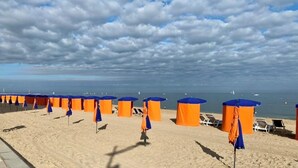 A beach with orange and blue beach umbrellas and lounge chairs, a sandy beach, and the ocean in the background. - 10 minutes walk from the sea, brand new wooden house for 4 to 6 people (Houlgate)