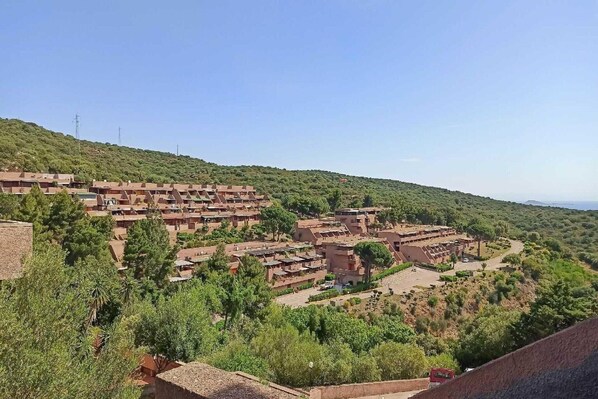 A hillside residential area with multiple buildings, including a large complex with multiple levels and a smaller structure with a courtyard. - Apartment in Olbia with shared garden (Olbia (SS))