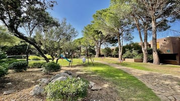 Un parque con árboles, una zona de juegos y un edificio al fondo.