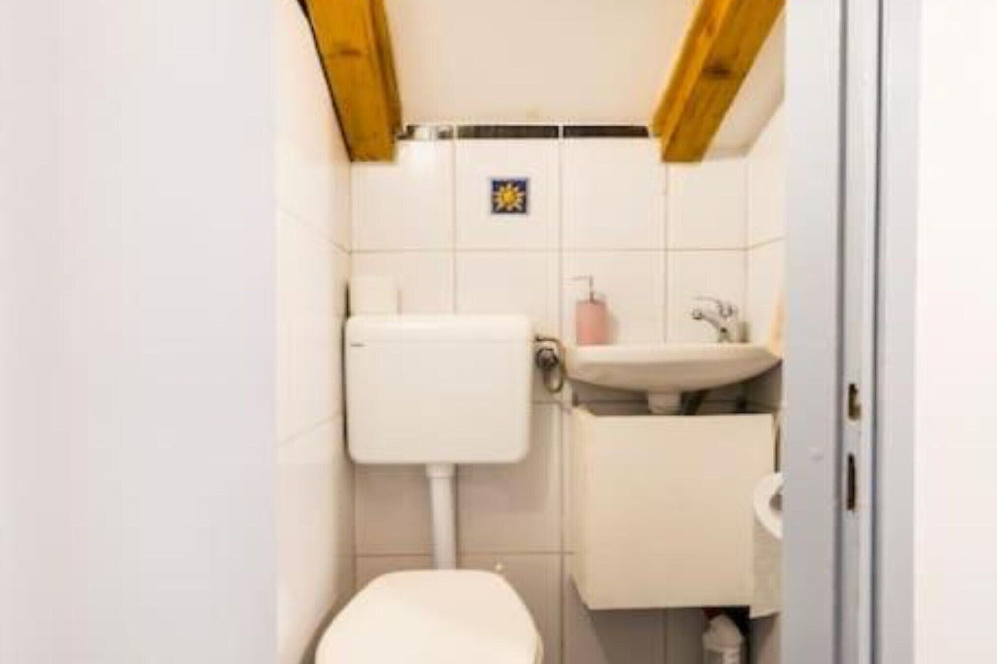 A small, compact bathroom with a toilet, sink, and storage cabinet.