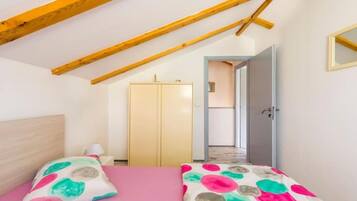 Un dormitorio con techo inclinado, una cama con colcha rosa, un armario y una puerta que da a otra habitación.