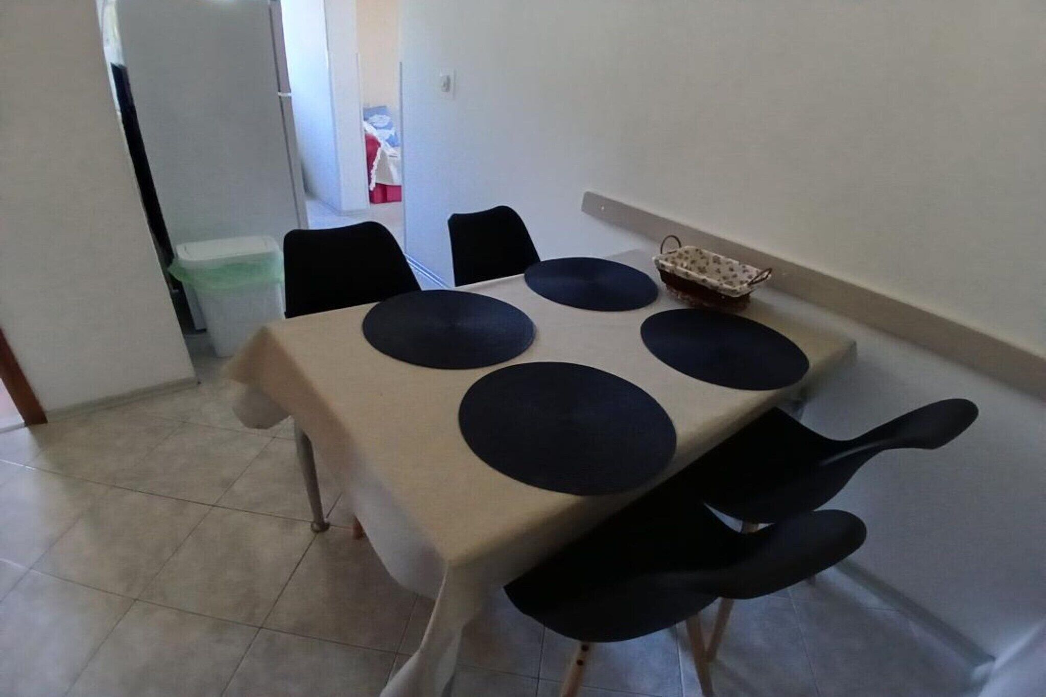 A dining table with a beige tablecloth and black circular placemats, surrounded by black chairs.