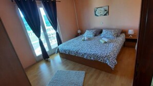 Un dormitorio con cama, mesita de noche, lámpara, ventana con cortinas y vista al exterior.