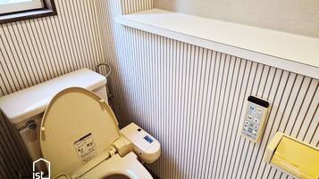 Ein kleines Badezimmer mit Toilette, einem Händetrockner und einem Regal über der Toilette.