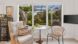 A room with a large window, wicker furniture, and a small table with a plant. - Comfortable & cosy unit w/ garden views (Queenscliff)