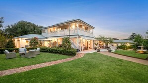 A two-story house with a covered patio, a well-maintained lawn, and outdoor seating. - Comfortable & cosy unit w/ garden views (Queenscliff)