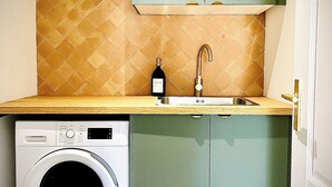 Une petite cuisine équipée d’un lave-linge, d’un évier et d’un meuble de rangement au-dessus du plan de travail.