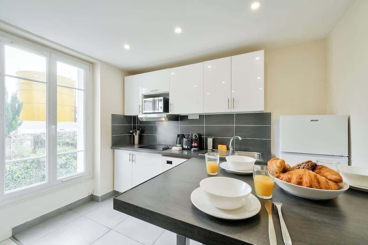 A modern kitchen with white cabinets, a black countertop, and a breakfast setup including croissants and orange juice.