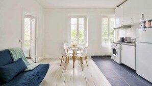A modern kitchen with white cabinets, a built-in washing machine, and a dining area with a table and chairs. - Quiet and cosy 2BR in Nanterre - Near La Defense (Nanterre)