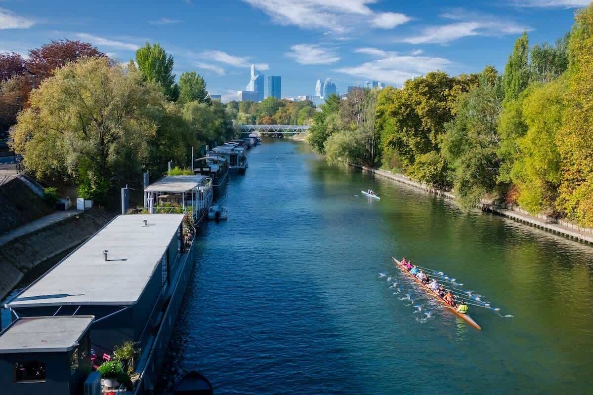 Um rio com uma corrida de barcos, uma ponte e um horizonte urbano ao fundo.