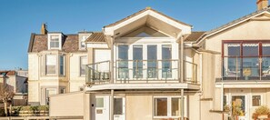 A two-story house with a balcony, a garage, and a visible front door. - West Cottage | Elie | 3 Bedroom Cottage (Elie)