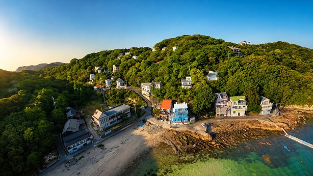 A coastal residential area with houses on a hillside, a beach, and a pier.