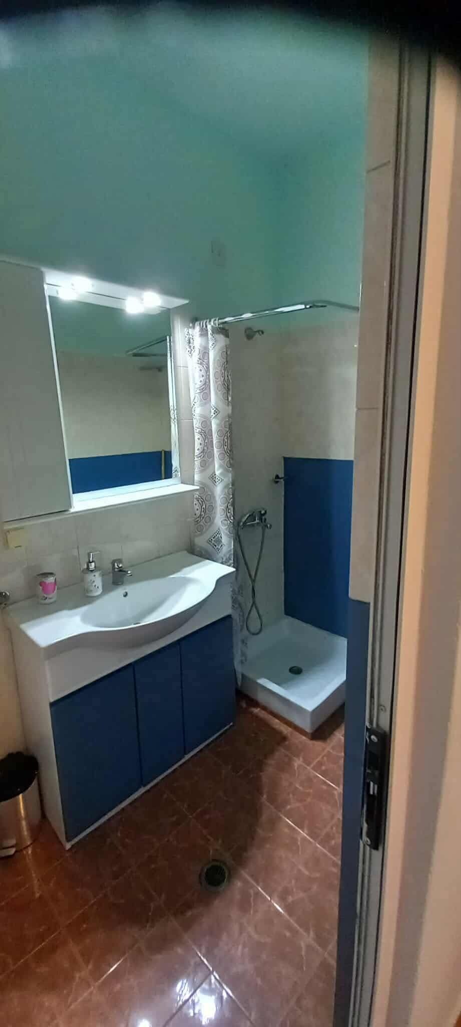 A bathroom with a sink, mirror, shower, and blue cabinets.