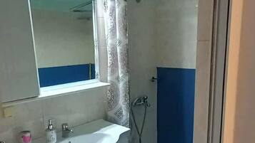 A bathroom with a sink, mirror, shower, and blue cabinets.
