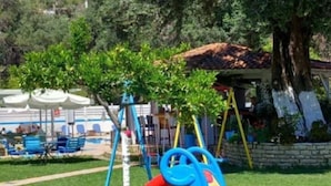A playground with slides and swings, surrounded by grass and trees. - Poseidon Apartments (Agios Gordios)