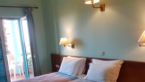 A hotel room with two beds, a sliding glass door to the balcony, and two wall-mounted lamps. - Poseidon Apartments (Agios Gordios)