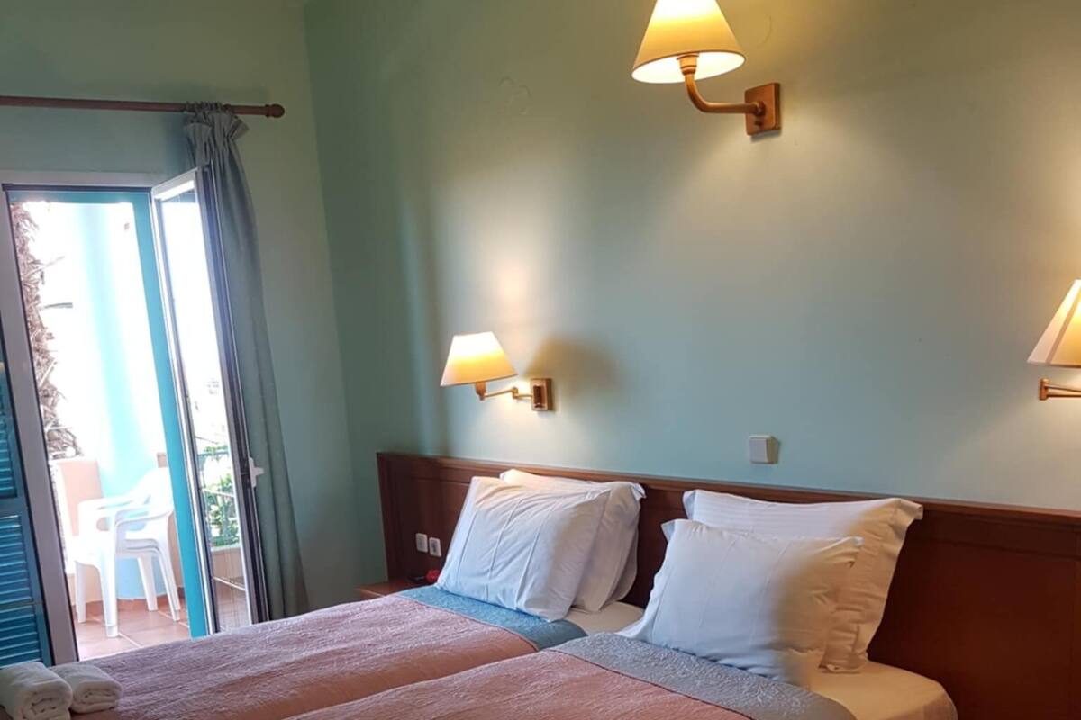 Ein Hotelzimmer mit zwei Betten, einer Schiebetür zum Balkon und zwei Wandleuchten.