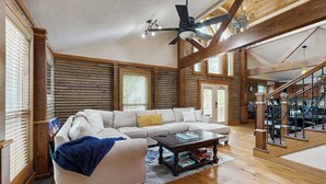 Un salon spacieux avec un grand canapé d’angle, des poutres en bois et un escalier.