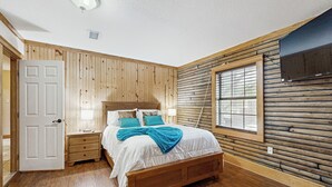 Une chambre à coucher avec un lit en bois, des tables de chevet, une fenêtre et un téléviseur fixé au mur.