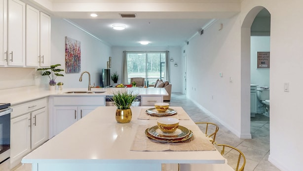 Una cucina moderna con mobili bianchi, un'isola centrale con ciotole con bordo dorato e una pianta in vaso.