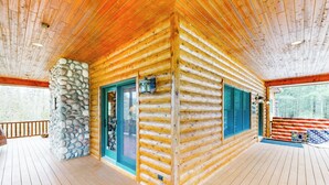A log cabin with a stone wall, wooden deck, and a large window. - Steps to Sturgeon River! Dog-Friendly Nature Haven (Vanderbilt)