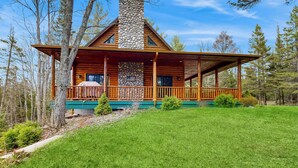 A log cabin with a stone chimney, wooden deck, and a covered porch. - Steps to Sturgeon River! Dog-Friendly Nature Haven (Vanderbilt)