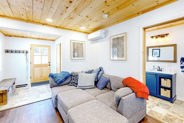 A living room with a grey sofa, wooden ceiling, and a blue cabinet with baskets. - Waterfront Escape on Long Lake! Ski, Paddle + Play (Madawaska)