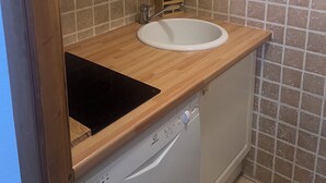 Cocina compacta con un lavamanos blanco, encimera de madera y lavavajillas.