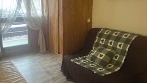 Una sala de estar acogedora, con piso de madera, un sofá oscuro con un cojín estampado, una puerta de madera y un cartel en la pared.