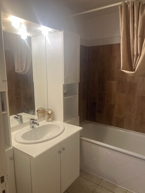 Een badkamer met een wit wastafelmeubel, een spiegel en een douchegedeelte.