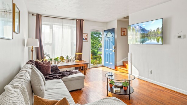 A modern living room with a sofa, coffee table, and a large TV. There is a door leading to a balcony with a view of greenery. - ❃Free Parking ❃ 2 King Beds ❃ Fenced Yard❃ ~ Floyd's Freedom ~ (Alexandria)