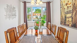 A dining area with a wooden table, chairs, a chandelier, a window with curtains, a potted plant, and a wall art piece. - ❃Free Parking ❃ 2 King Beds ❃ Fenced Yard❃ ~ Floyd's Freedom ~ (Alexandria)