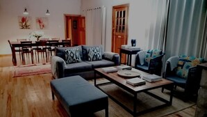 A living room with a sofa, a coffee table, and a dining area with chairs and a table. - Self-catering farmhouse on working farm, a peaceful retreat outside of Underberg (Underberg)