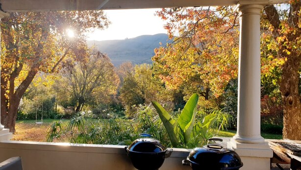 A view from a covered porch with a pergola, overlooking a garden with trees and a distant mountain. - Self-catering farmhouse on working farm, a peaceful retreat outside of Underberg (Underberg)