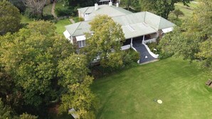 A large, two-story house with a green roof, surrounded by lush greenery and a well-maintained lawn. - Self-catering farmhouse on working farm, a peaceful retreat outside of Underberg (Underberg)