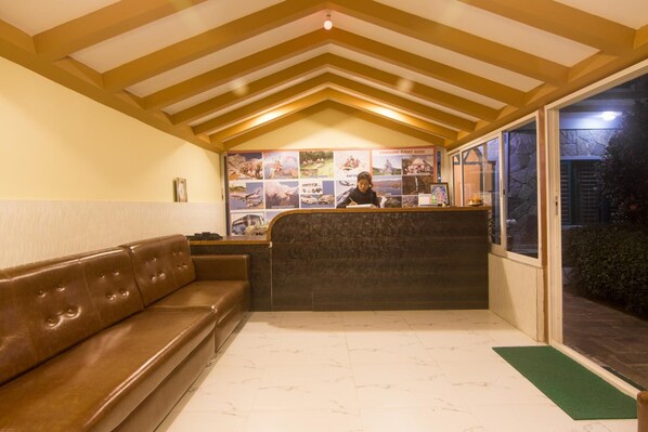 A reception area with a brown leather bench, a reception desk, and a wall displaying various photos. - Hotel Noble Inn (Pokhara)