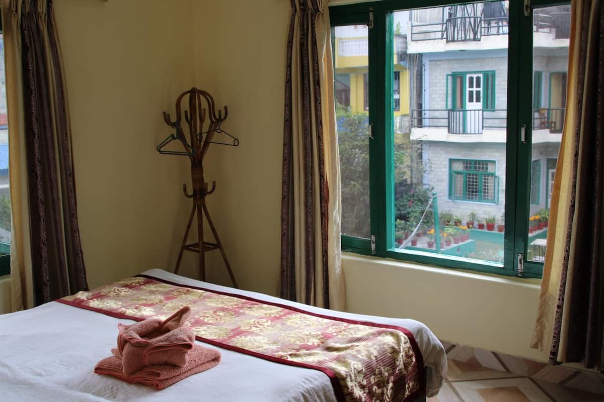 A hotel room with a bed, a window with a view of buildings, and a coat rack.