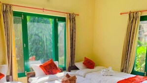 Habitación de hotel con dos camas, ventanas con marco verde y cortinas.