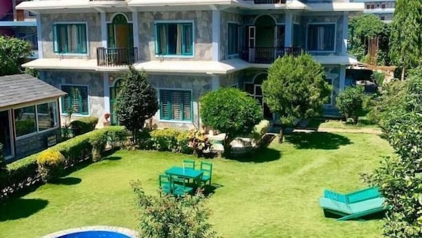 Un hotel de varios pisos con un letrero que dice "Hotel Noble Inn". Cuenta con un césped bien cuidado, una piscina y asientos al aire libre.